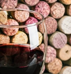 Glass of red wine in front of a background of corks