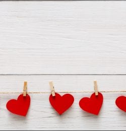 Red paper hearts row border on clothespins on white rustic wood planks