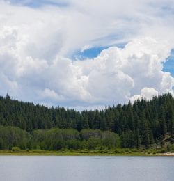 Lake Tahoe Cloudscape – dramatic clouds over Lake Tahoe showing smooth blue water, lush green evergreens, and ample copy space in the upper half of the frame. Lake Tahoe is a very popular U.S. tourist destination, famous for its clear water, natural beauty, year-round recreational opportunities, and proximity to Northern California.